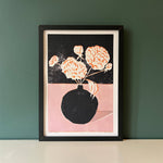 Framed artwork of a vase with flowers on a dark background, displayed against a green wall.