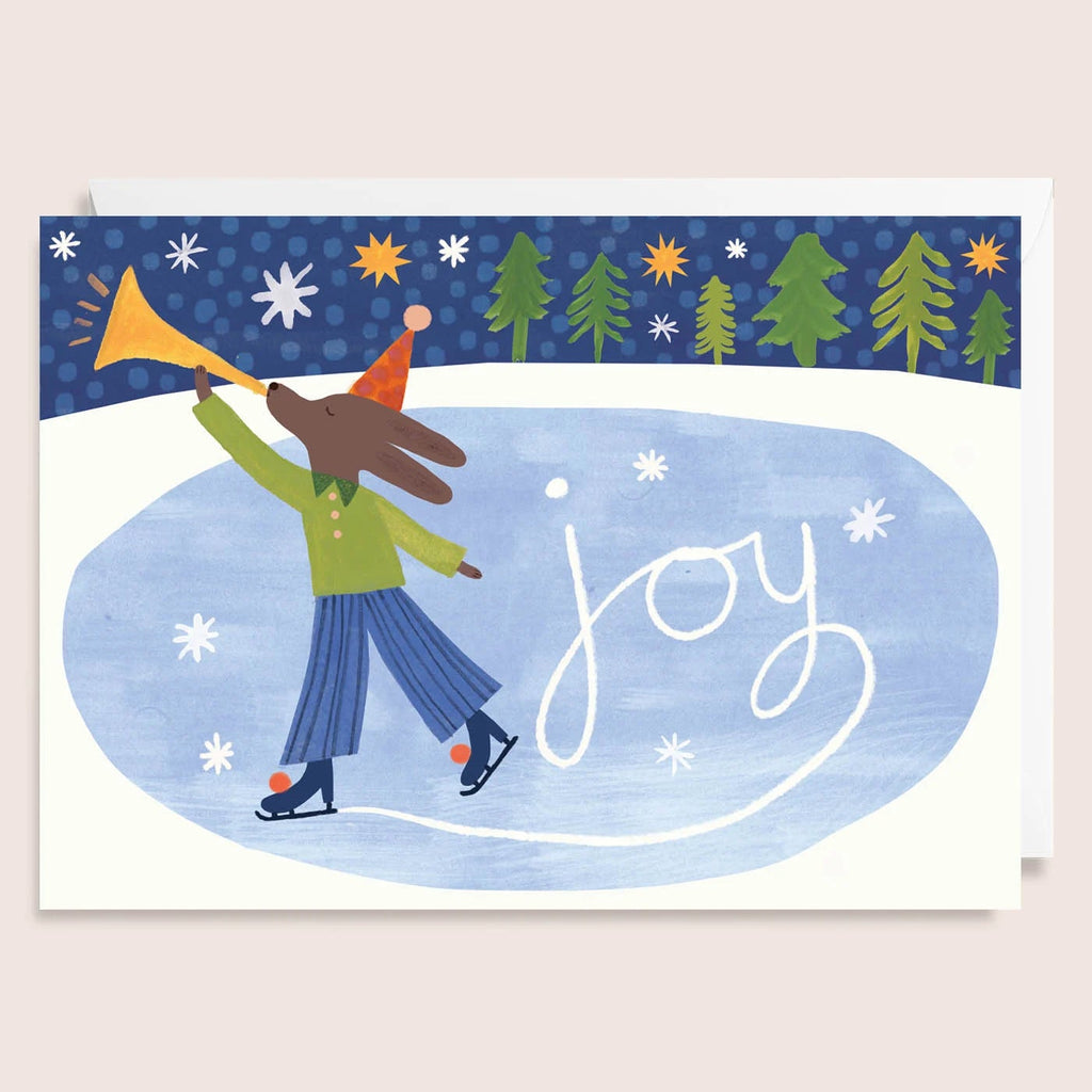 Card with an iceskating dog playing a horn, trees, and the word 'joy' on a blue background.