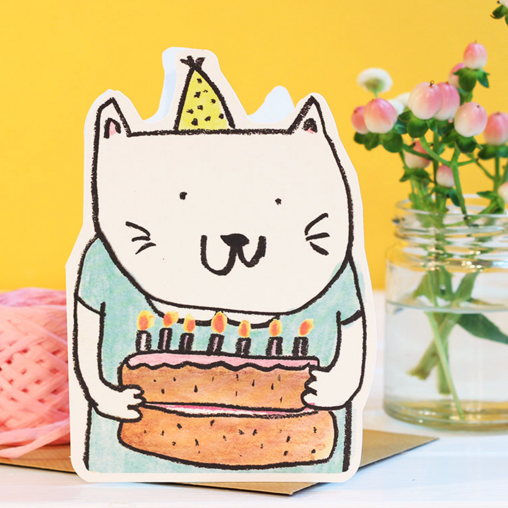 Card with a cat holding a birthday cake and candles against a yellow background