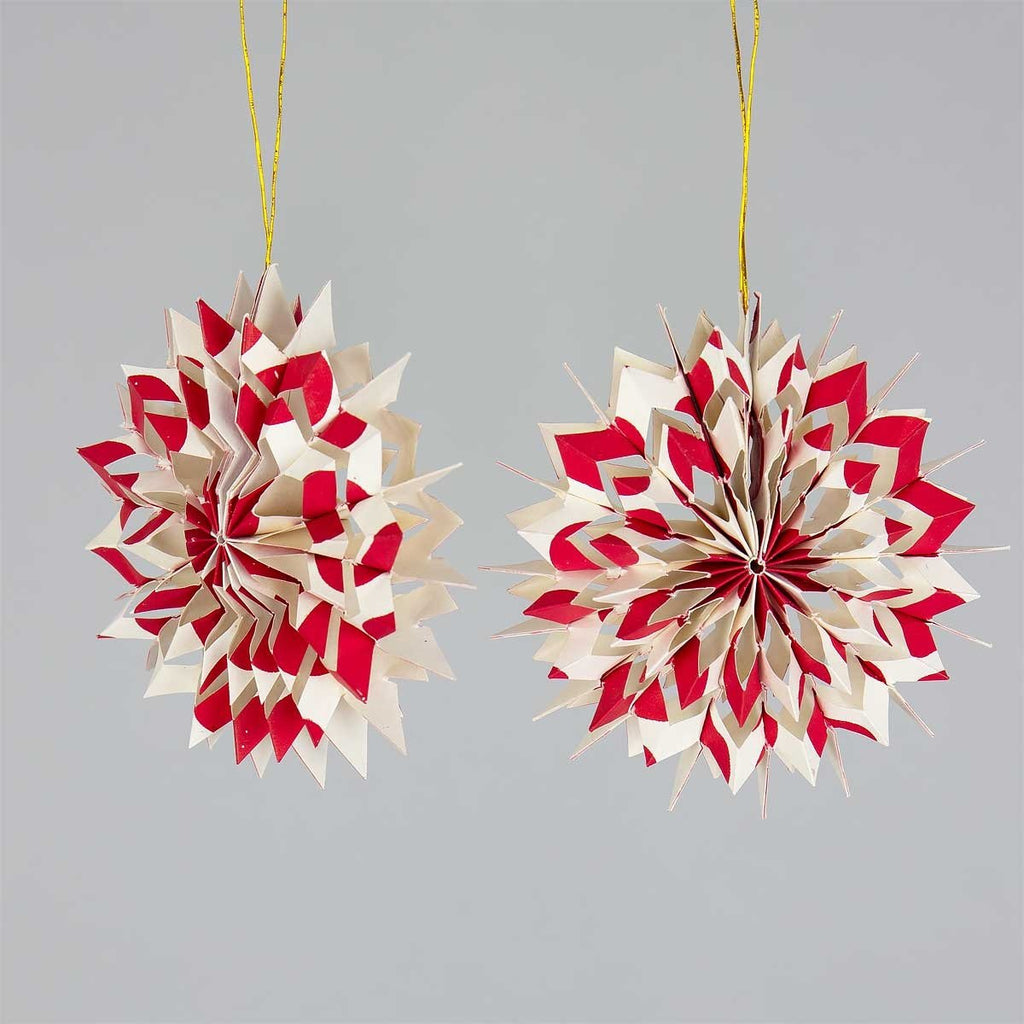 Two red and beige paper star decorations hanging against a gray background