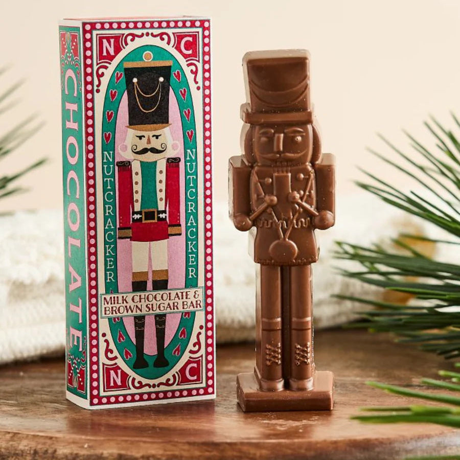 Chocolate nutcracker figurine next to its packaging on a wooden surface with a neutral background