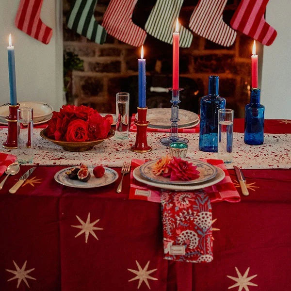 Decorative Christmas table setting with stockings, candles, and a fireplace in the background.