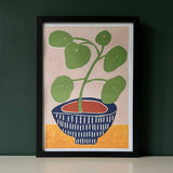 Framed artwork of a potted plant on a beige background with a dark green wall.
